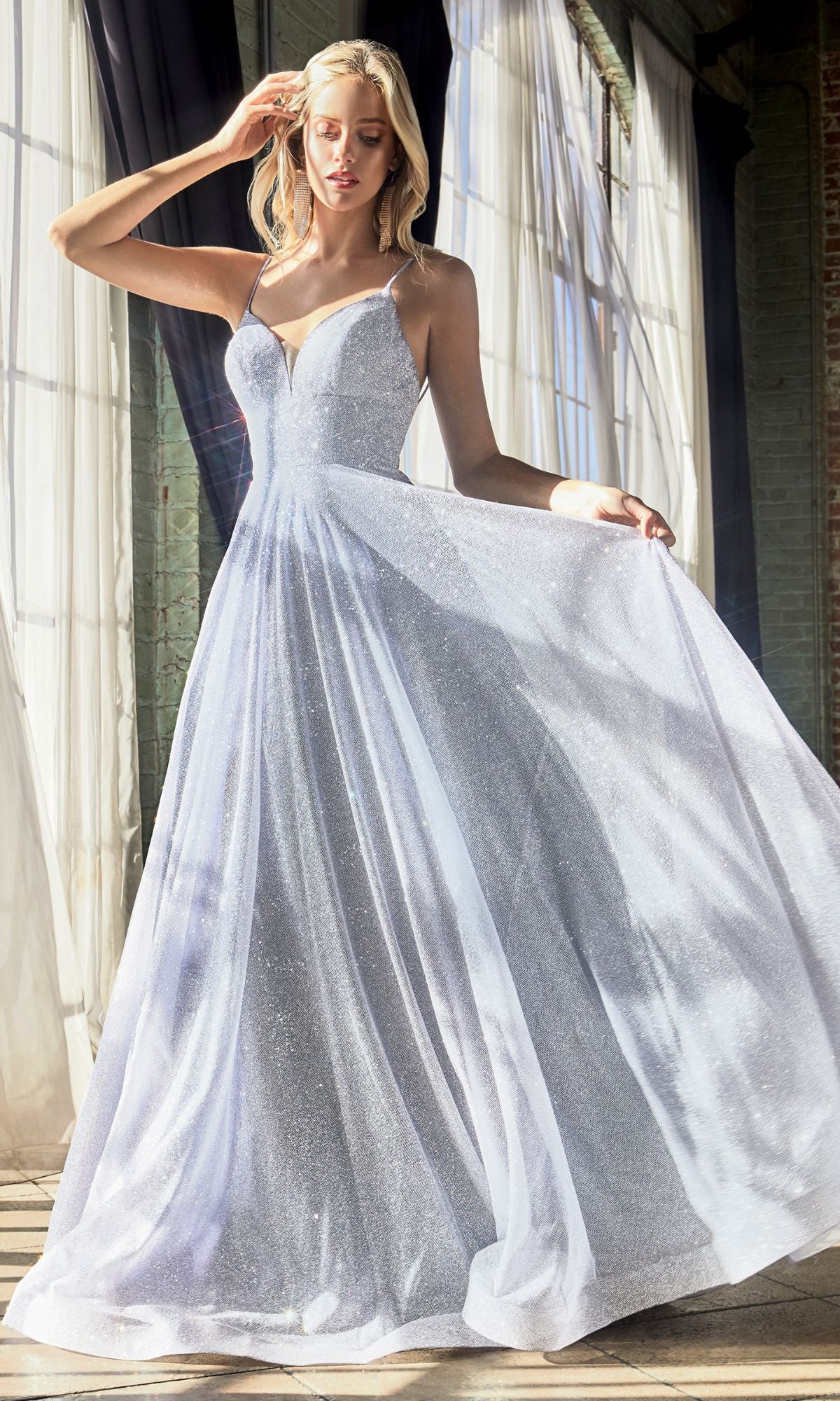 A woman in a Light Blue Glitter Long A-Line Prom Dress CD205 with a sleeveless design and full skirt stands in sunlight by tall windows and dark curtains.